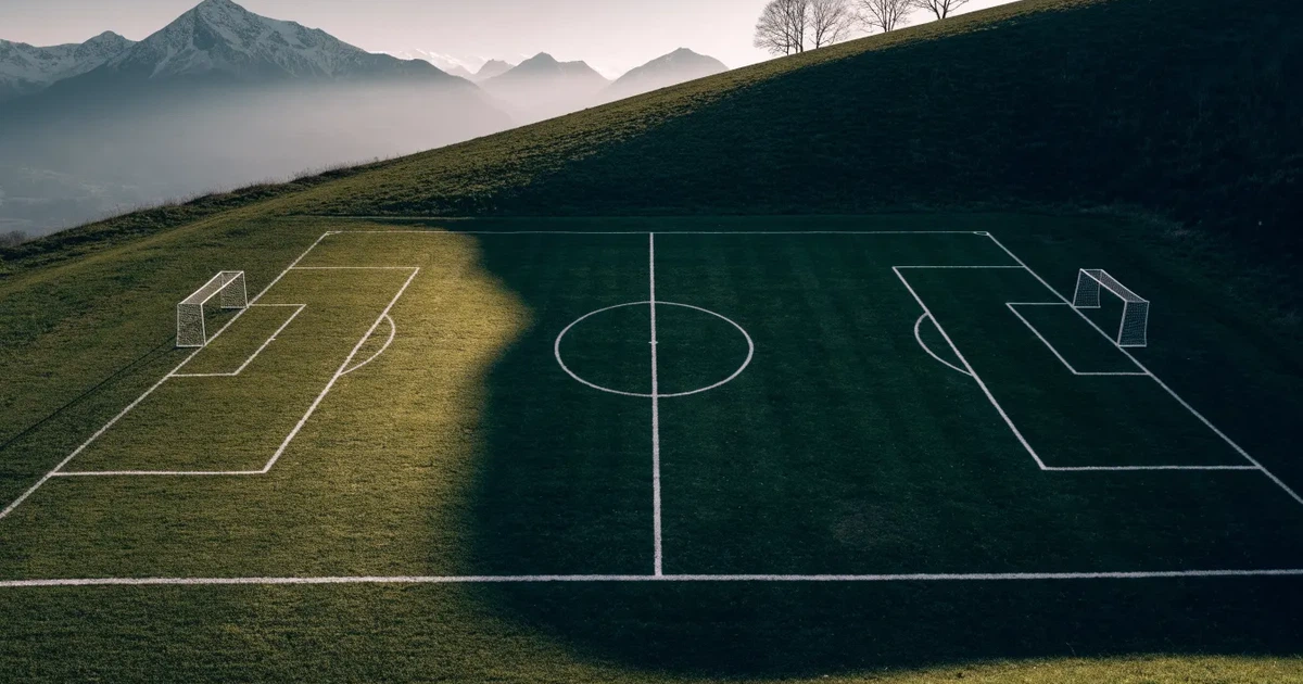 Ein Fussballplatz aus der Vogelperspektive mit sauberen Linien auf dichtem Rasen, in der Ferne verschneite Berge.