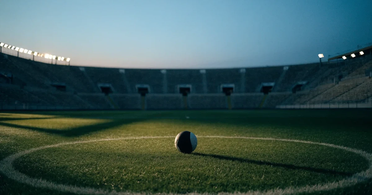 Ein Fussball liegt auf dem Mittelpunkt eines leeren Rasens, im Hintergrund steigen steile Tribünen in der Dämmerung auf.