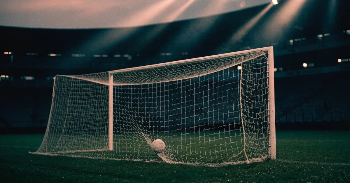 Ein Fussball liegt im Netz eines Tores, Flutlicht und kalte Abendluft liegen über dem leeren Platz